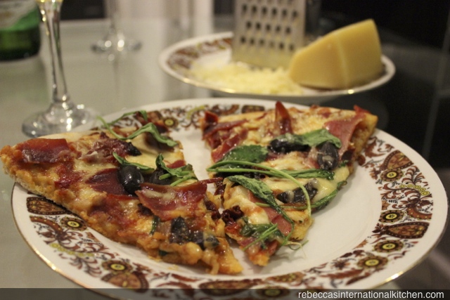 Recipe for homemade pizza with prosciutto, olives, sun-dried tomatoes, and arugula. 
